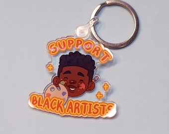 May include: A clear acrylic keychain with a colorful illustration of a person with paint on their face and the text "Support Black Artists".