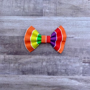 May include: A rainbow striped bow tie with orange, yellow, green, purple, and red stripes. The bow tie is made of fabric and has a classic bow shape.