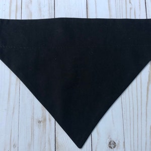 Pode incluir: Uma bandana preta lisa para cães. A bandana é triangular e tem uma borda branca costurada.