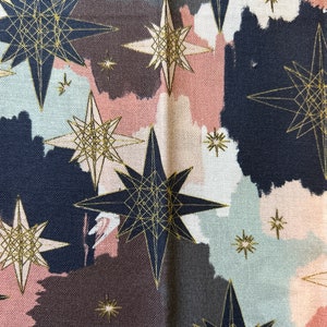 May include: A fabric with a repeating pattern of gold stars on a background of pink, brown, and blue watercolor-like shapes.