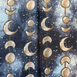 May include: A dark blue fabric with a repeating pattern of gold crescent moons and circles. The fabric has a subtle starry sky design.