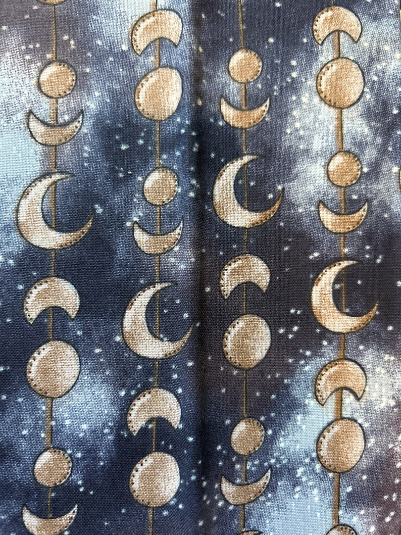 May include: A dark blue fabric with a repeating pattern of gold crescent moons and circles. The fabric has a subtle starry sky design.