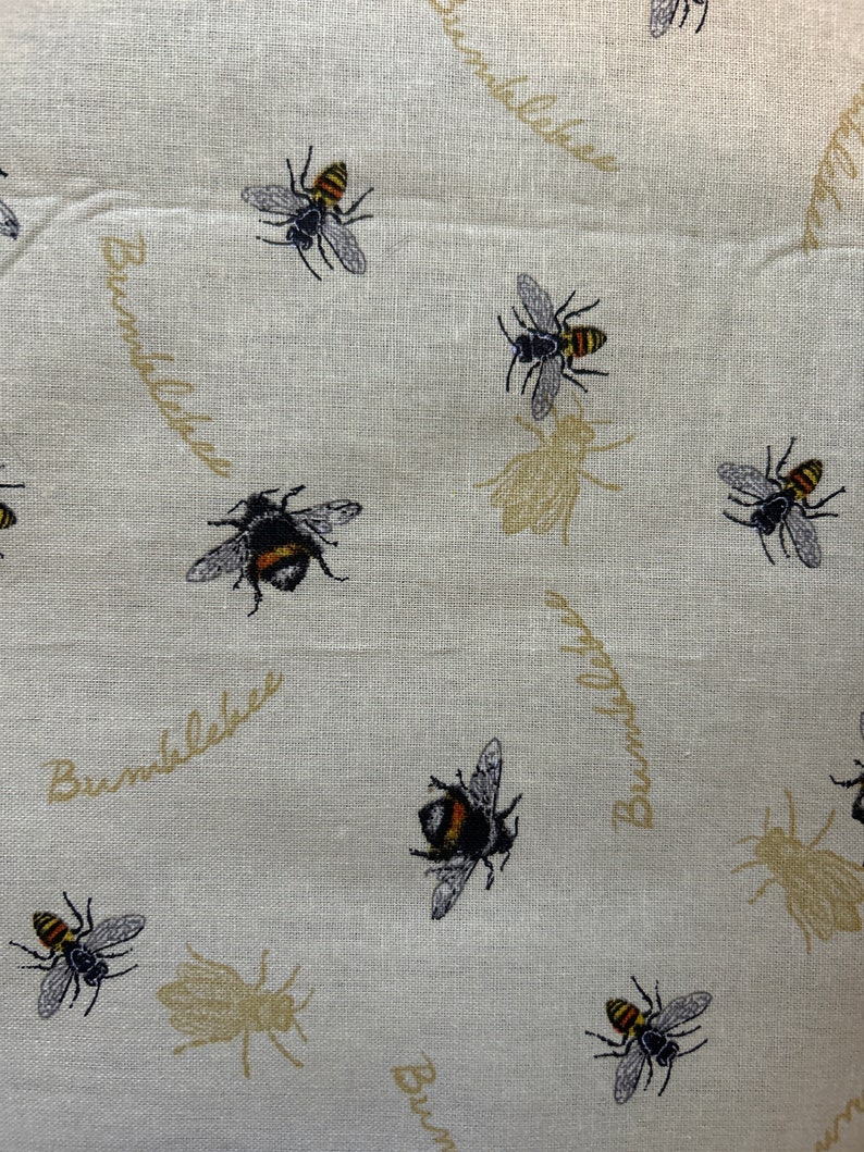 May include: A white fabric with a repeating pattern of bumblebees and the text "Bumblebee" in a script font. The bumblebees are black and yellow with brown wings.