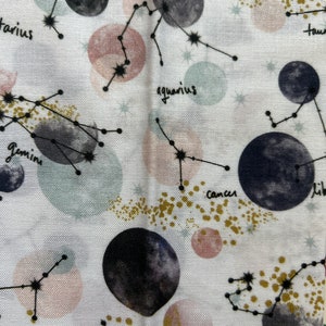 May include: White fabric with a repeating pattern of constellations and planets. The constellations are outlined in black and the planets are painted in shades of gray and pink. The constellations are labeled with their astrological signs: Capricorn, Aquarius, Pisces, Taurus, Gemini, Cancer, Libra, Scorpio.
