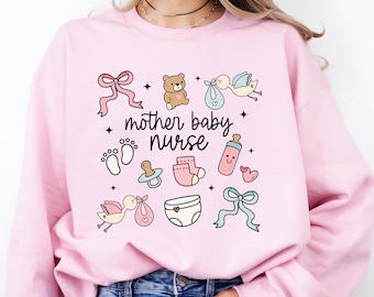 Könnte beinhalten: Ein hellrosa Sweatshirt mit dem Text "mother baby nurse" und babybezogenen Illustrationen, darunter ein Teddybär, ein Schnuller, eine Windel und eine Babyflasche.