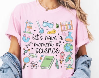 Pode incluir: Camiseta rosa claro com a frase "let's have a moment of science" e gráficos com tema científico. Os gráficos incluem um microscópio, um foguete, um globo e um livro com a etiqueta "science".