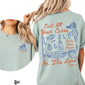 K&ouml;nnte beinhalten: Hellgr&uuml;nes T-Shirt mit einem Angelmotiv. Auf der R&uuml;ckseite steht der Text "Cast All Your Cares On The Lord" mit blauen und orangefarbenen Angelillustrationen. Auf der Vorderseite befindet sich eine kleine Fischernetz- und Fischgrafik.