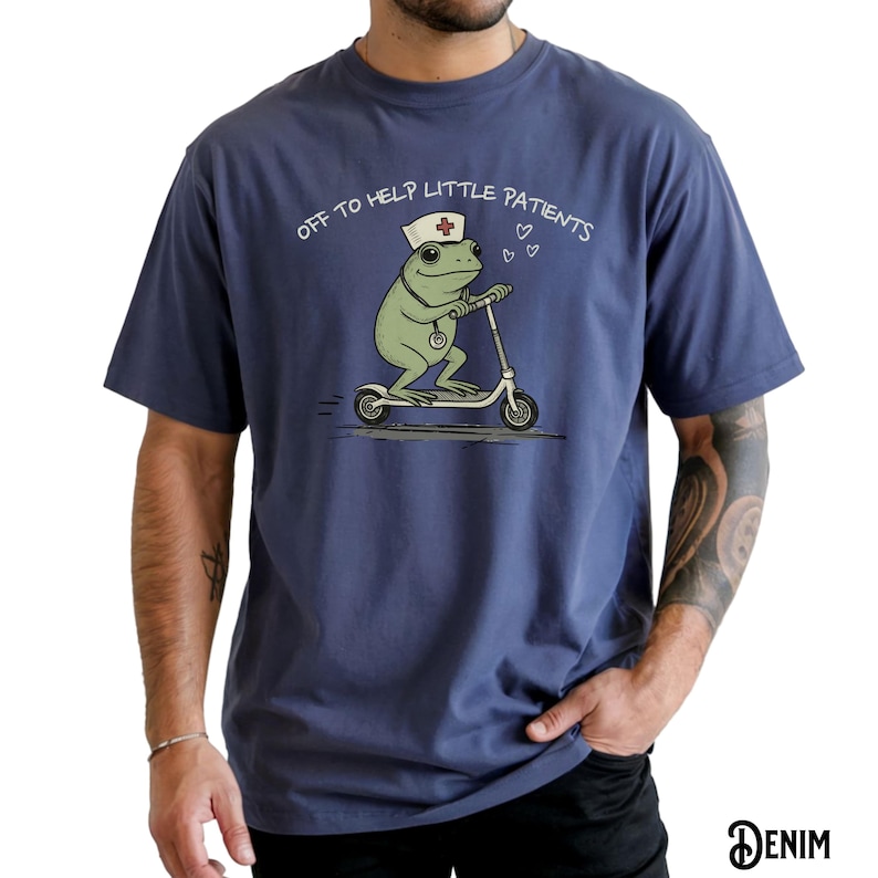May include: A navy blue t-shirt featuring a cartoon frog wearing a nurse's cap and riding a scooter. The frog has a stethoscope and the text "OFF TO HELP LITTLE PATIENTS" is above the frog. The word "DENIM" is at the bottom right.