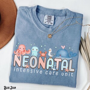 May include: A light blue t-shirt featuring a graphic of sea creatures and the text "NEONATAL intensive care unit".