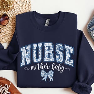 Könnte beinhalten: Navyblauer Sweatshirt mit einem weißen Blumenmuster, auf dem "NURSE mother baby" mit einer blauen Schleife steht.