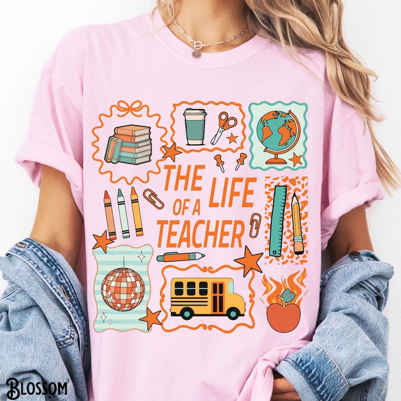 May include: Pink t-shirt with a colorful graphic design featuring school-related icons and the text "THE LIFE OF A TEACHER". The design includes a globe, school bus, apple, and other school supplies.