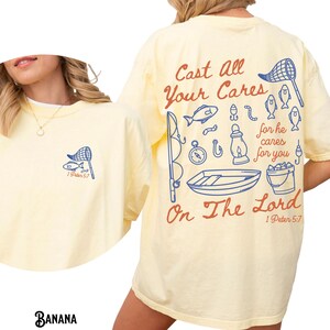 K&ouml;nnte beinhalten: Hellgelbes T-Shirt mit einem Angelmotiv. Auf der Vorderseite befindet sich ein kleines blaues Netz- und Fischdesign mit dem Text "1 Peter 5:7". Auf der R&uuml;ckseite befindet sich ein gr&ouml;&szlig;eres Design mit dem Text "Cast All Your Cares On The Lord 1 Peter 5:7."