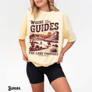 May include: A yellow t-shirt with a graphic print of a desert landscape with a sunset and the text "Where the Lord Guides, The Lord Provides, Isaiah 58:11".