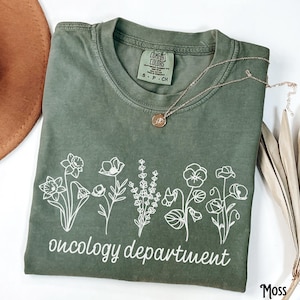 May include: A green t-shirt with a white graphic of flowers and the text "oncology department".