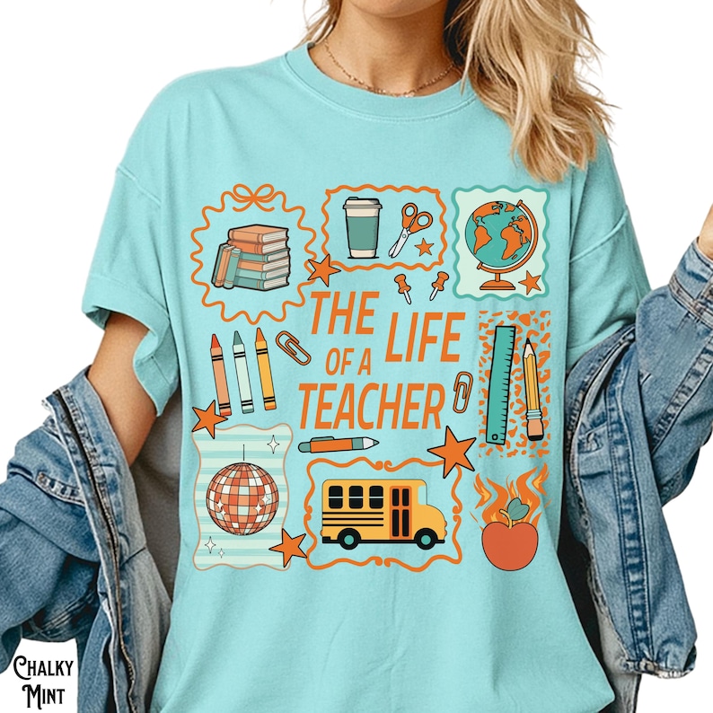 May include: A light blue t-shirt with the text "THE LIFE OF A TEACHER" and various school-themed graphics. The graphics include books, a coffee cup, scissors, a globe, pencils, a ruler, a school bus, and an apple.