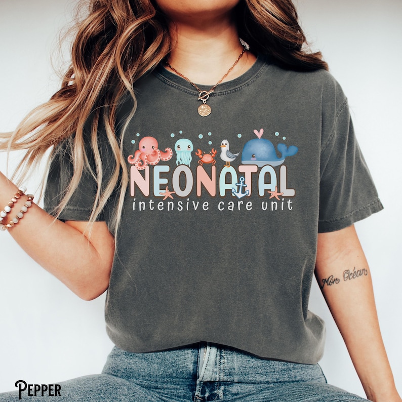May include: A dark grey t-shirt with a graphic of sea creatures and the text "Neonatal Intensive Care Unit".