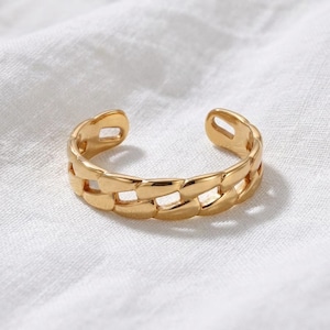 Puede incluir: Un anillo abierto de tono dorado con un diseño de eslabones de cadena pulidos. La banda está construida con eslabones metálicos ovalados interconectados con una superficie lisa y reflectante. El anillo tiene una abertura en la parte superior.