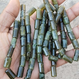 以下が含まれることがあります： 濃い緑色の宝石ビーズのストランド。各ビーズは、わずかに不規則な形状のファセットカットされた円柱です。