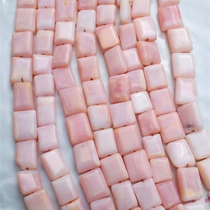 May include: A strand of pink and white square-shaped shell beads. The beads have a smooth, polished finish and a slight iridescent sheen.