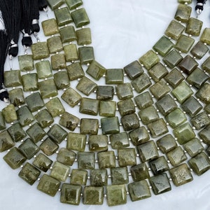 May include: A strand of green gemstone beads, each bead is square shaped and has a slightly irregular, faceted surface. The beads are strung on silver wire.