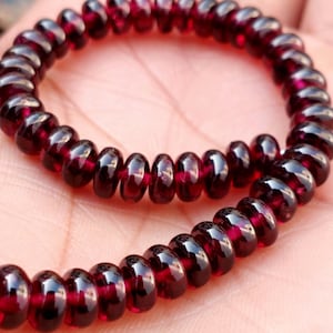 May include: A red gemstone bracelet made of small, round beads. The bracelet is made of many beads and is coiled on a hand.