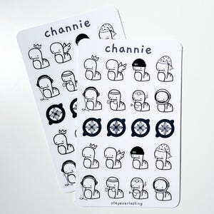 K&ouml;nnte beinhalten: Zwei Stickerb&ouml;gen mit schwarz-wei&szlig;en Illustrationen. Die Aufkleber zeigen eine Cartoonfigur in verschiedenen Outfits, darunter eine Krone, Engelsfl&uuml;gel und ein Weltraumhelm. Das Wort "channie" ist oben auf jedem Bogen aufgedruckt, und "stayeverlasting" ist unten auf einem Bogen aufgedruckt.