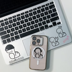 May include: A clear phone case with a cartoon character design rests on a laptop. The laptop has stickers with similar cartoon characters. The word "stay" is written in pink on the laptop.