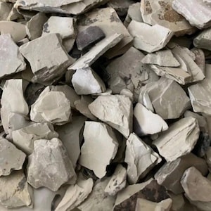 May include: A collection of irregular, flat, and jagged stone fragments in shades of light beige, tan, and off-white. The pieces vary in size and shape, featuring rough, matte textures and sharp, broken edges layered densely across the frame.