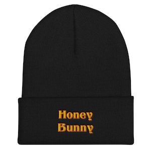 Könnte beinhalten: Schwarze Mütze mit dem Text "Honey Bunny" in Orange und Gelb gestickt.