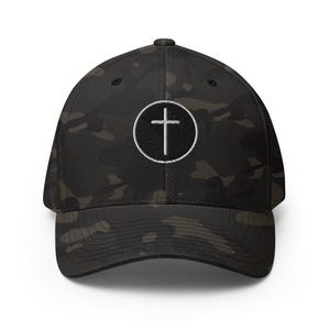 May include: A black camouflage baseball cap with a white embroidered cross inside a circle on the front. The cap has a curved brim and a structured fit, suitable for various outdoor activities.