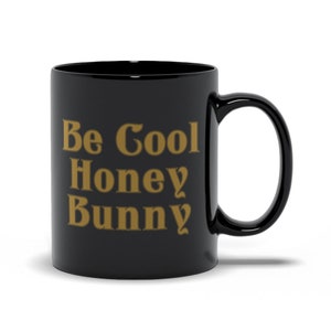 May include: Black ceramic coffee mug with the text "Be Cool Honey Bunny" in gold lettering.
