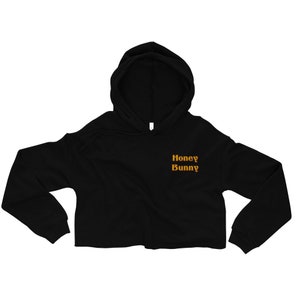 May include: Black cropped hoodie with a long sleeve and a hood. The hoodie has the text "Honey Bunny" embroidered on the front in orange.