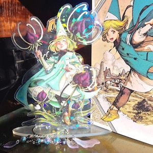 May include: A clear acrylic standee featuring a cartoon character in a light blue outfit, holding a staff with a purple flower. The standee has a holographic effect. A second character is depicted on a card in the background.