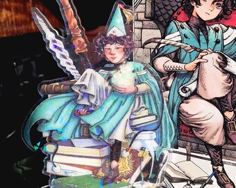 May include: A clear acrylic standee featuring a seated figure in teal robes and a pointed hat, holding a glowing orb. The figure is perched atop a stack of books. A second illustration of a similar figure is visible to the right.