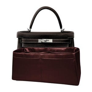 May include: A dark brown leather handbag with a top handle and silver-tone hardware. The bag has a structured design with white stitching and a matching dark brown interior organizer.