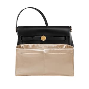 May include: Black leather handbag with a top handle and gold-tone hardware. The bag features a flap closure with a circular clasp. A beige fabric organizer is inside the bag, with multiple pockets.