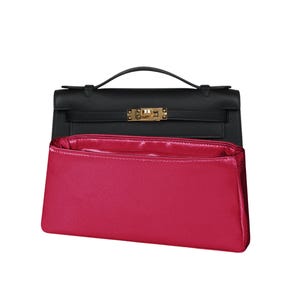 May include: A black leather handbag with a gold-toned metal clasp and a top handle, positioned behind a bright magenta rectangular fabric bag organiser insert that features a smooth, satin-like finish and a structured, open-top design.