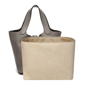 May include: A gray leather tote bag with a matching interior organizer. The tote features a structured design with a top handle and a rectangular shape. The interior organizer is a light beige color and fits inside the tote.