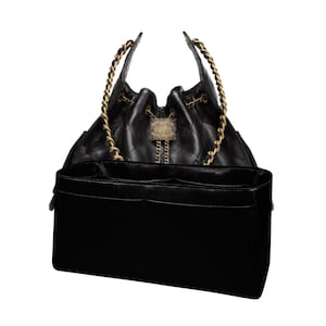 Könnte beinhalten: Schwarze, gesteppte Lederhandtasche mit goldfarbenen Kettenriemen und Kordelzugverschluss. Die Tasche hat eine dekorative goldfarbene Verzierung und einen schwarzen Innenorganizer.