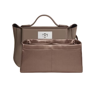 May include: A taupe-colored handbag with a top handle and a silver-tone clasp. The bag has a structured design with a matching interior organizer. The interior organizer has multiple pockets for storage.