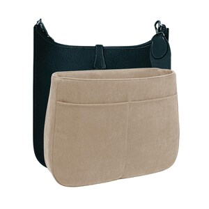 Puede incluir: Un bolso de hombro de cuero negro con un inserto organizador de fieltro beige. El bolso tiene forma curva con correa y cierre de hebilla. El organizador tiene múltiples bolsillos.