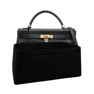 May include: A black textured leather handbag with a gold-tone lock and handle, positioned behind a black felt bag organizer insert featuring multiple interior compartments for structured storage and organization.