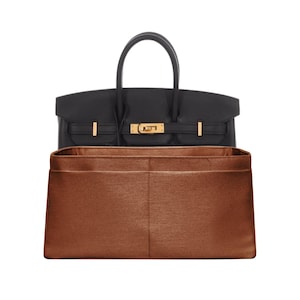 Può includere: Borsa in pelle nera con manico superiore e finiture color oro. All'interno della borsa è presente un organizer in feltro marrone. La borsa ha una chiusura con patta e chiusura a girello. L'organizer ha più tasche.