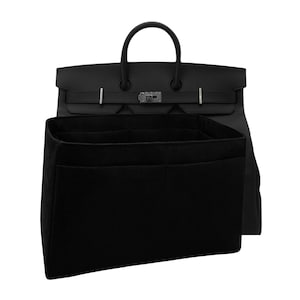 May include: A black felt handbag organiser insert with multiple interior compartments positioned in front of a black leather handbag featuring dual top handles, a flap closure, and silver-toned metal hardware accents on the front strap.