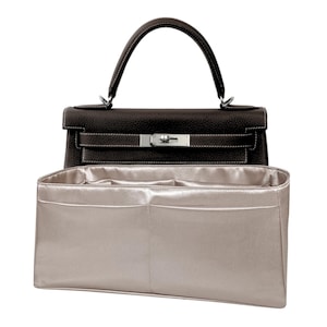 May include: A beige felt bag organizer with multiple compartments for a handbag. The organizer has a smooth, satin-like finish.