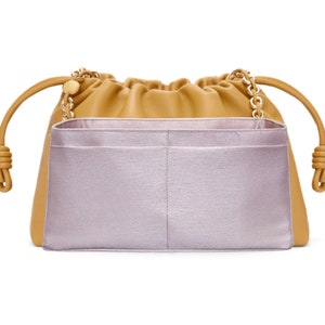 May include: A tan leather drawstring bag with a light purple fabric organiser insert. The bag features gold chain straps and knotted leather handles. The organiser has multiple compartments.