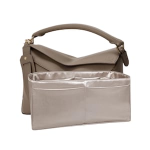 May include: A taupe leather handbag with a top handle and a matching interior organiser. The bag has a structured design with a flap closure and gold-tone hardware. The organiser is a light champagne colour with multiple compartments.
