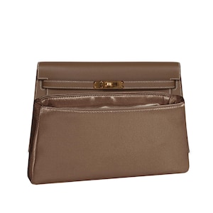 May include: A taupe-colored handbag with a structured design. The bag features a top flap with a gold-tone clasp and stitching details. The interior is visible, showcasing a matching satin lining.