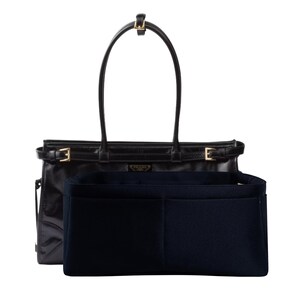 May include: Black leather tote bag with gold-tone hardware, featuring a top handle and a rectangular shape. Includes a navy blue felt organizer insert with multiple compartments. The bag has a subtle logo detail.