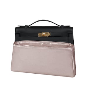 May include: A black leather handbag with a gold-toned metal clasp and a single top handle, positioned behind a rectangular, metallic light pink fabric bag organizer insert with a smooth, satin-like finish and a structured, open-top design.